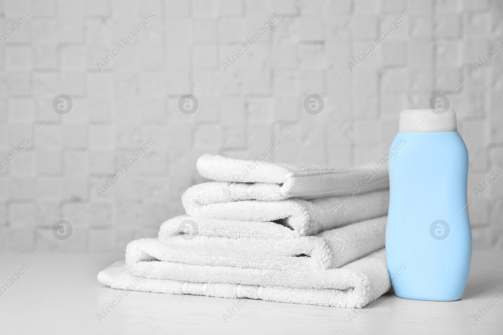 Photo of Bottle with shampoo and soft bath towels on table