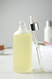 Photo of Bottle of hydrophilic oil and pipette on white table