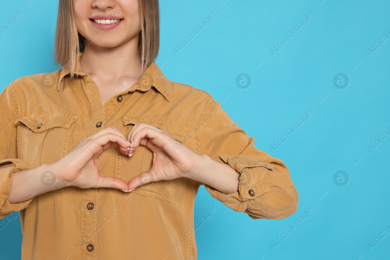 Photo of Young woman making heart with hands on turquoise background, space for text. Volunteer concept