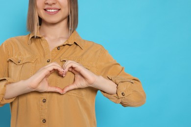 Young woman making heart with hands on turquoise background, space for text. Volunteer concept