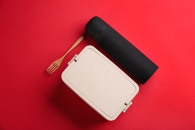 Thermos and lunch box with fork on red background, flat lay
