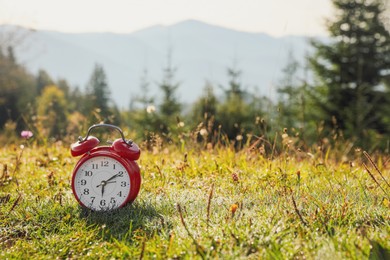 Red alarm clock on grass outdoors in morning, space for text