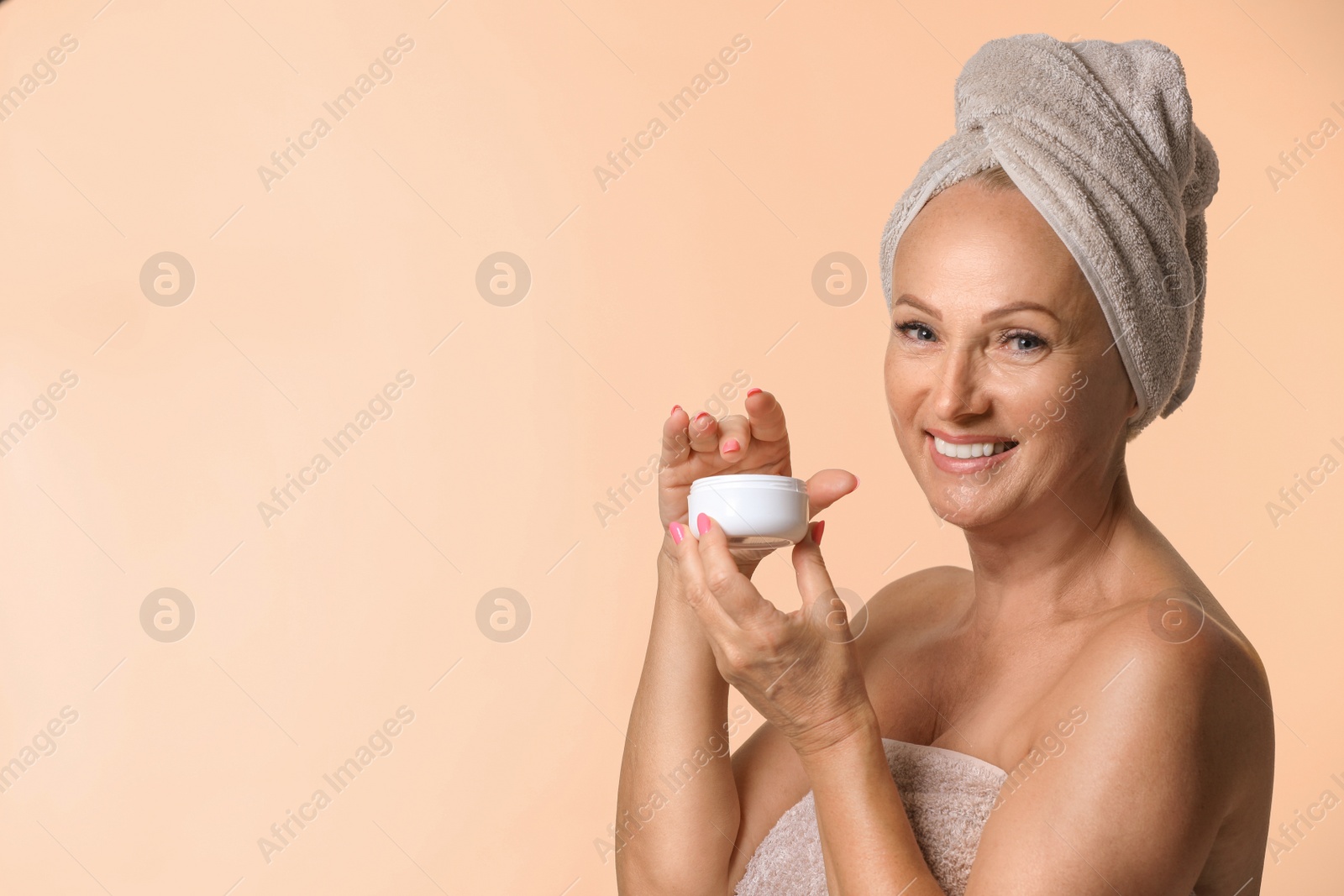 Photo of Portrait of beautiful mature woman with perfect skin holding jar of cream on beige background. Space for text