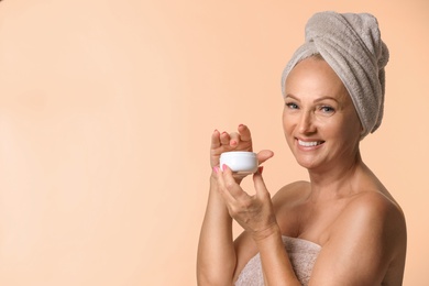 Photo of Portrait of beautiful mature woman with perfect skin holding jar of cream on beige background. Space for text