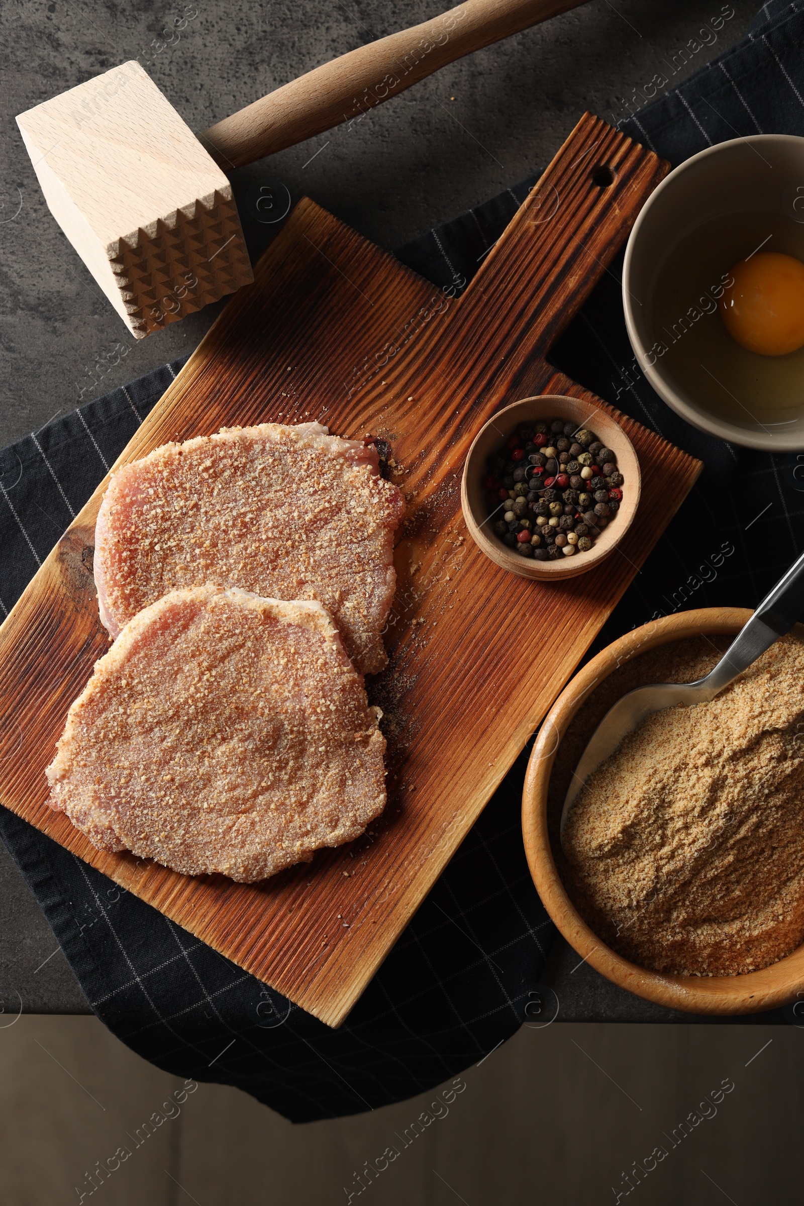 Photo of Cooking schnitzel. Raw breaded pork slices, meat tenderizer and ingredients on grey table, flat lay