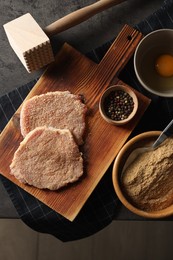 Cooking schnitzel. Raw breaded pork slices, meat tenderizer and ingredients on grey table, flat lay
