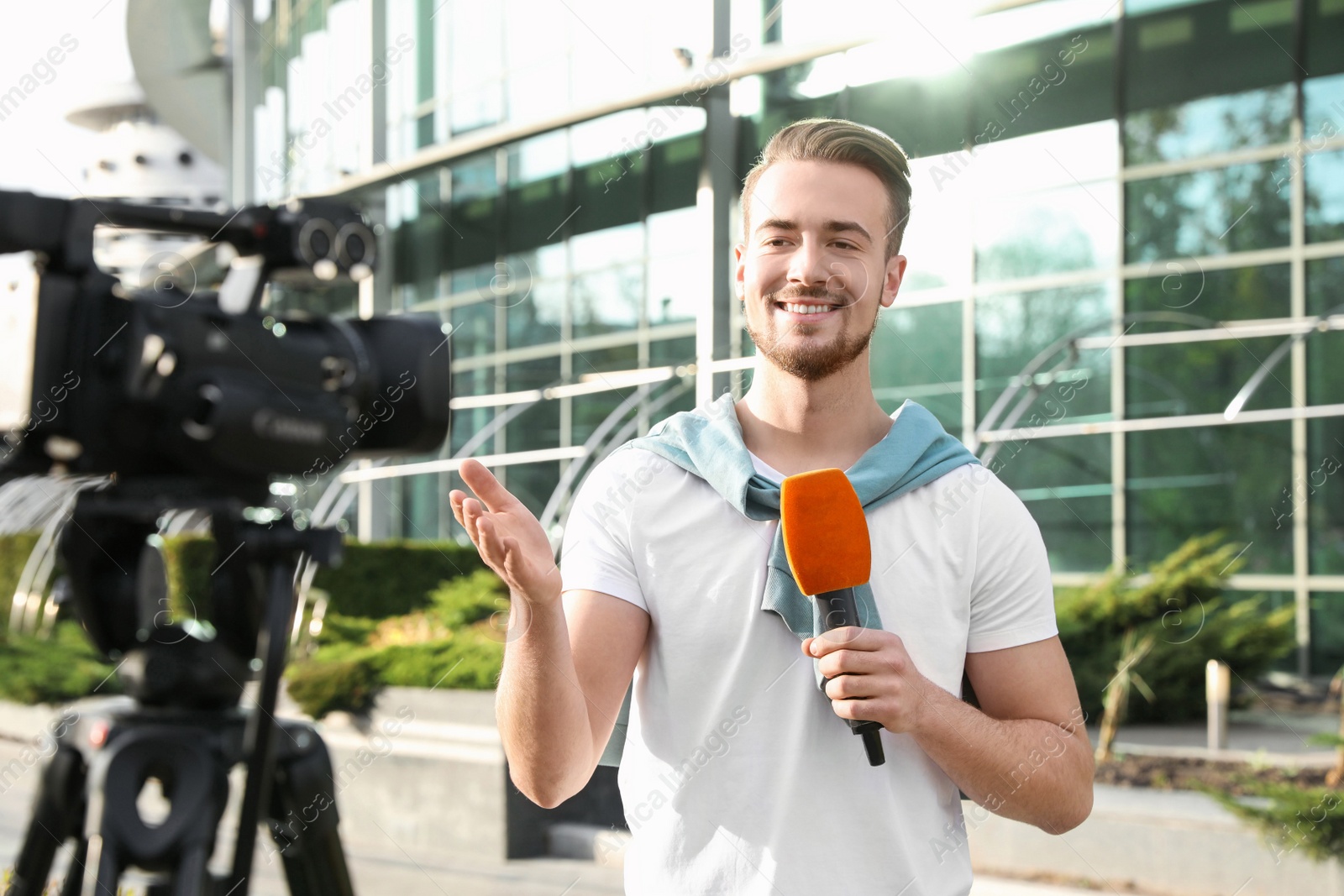 Photo of Young male journalist with microphone working on city street