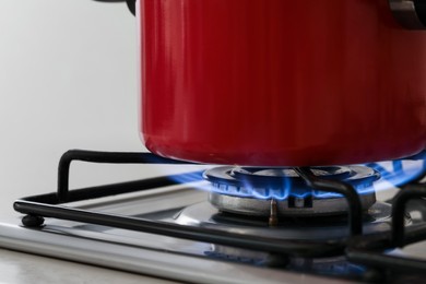 Photo of Red pot on stylish kitchen stove with burning gas, closeup
