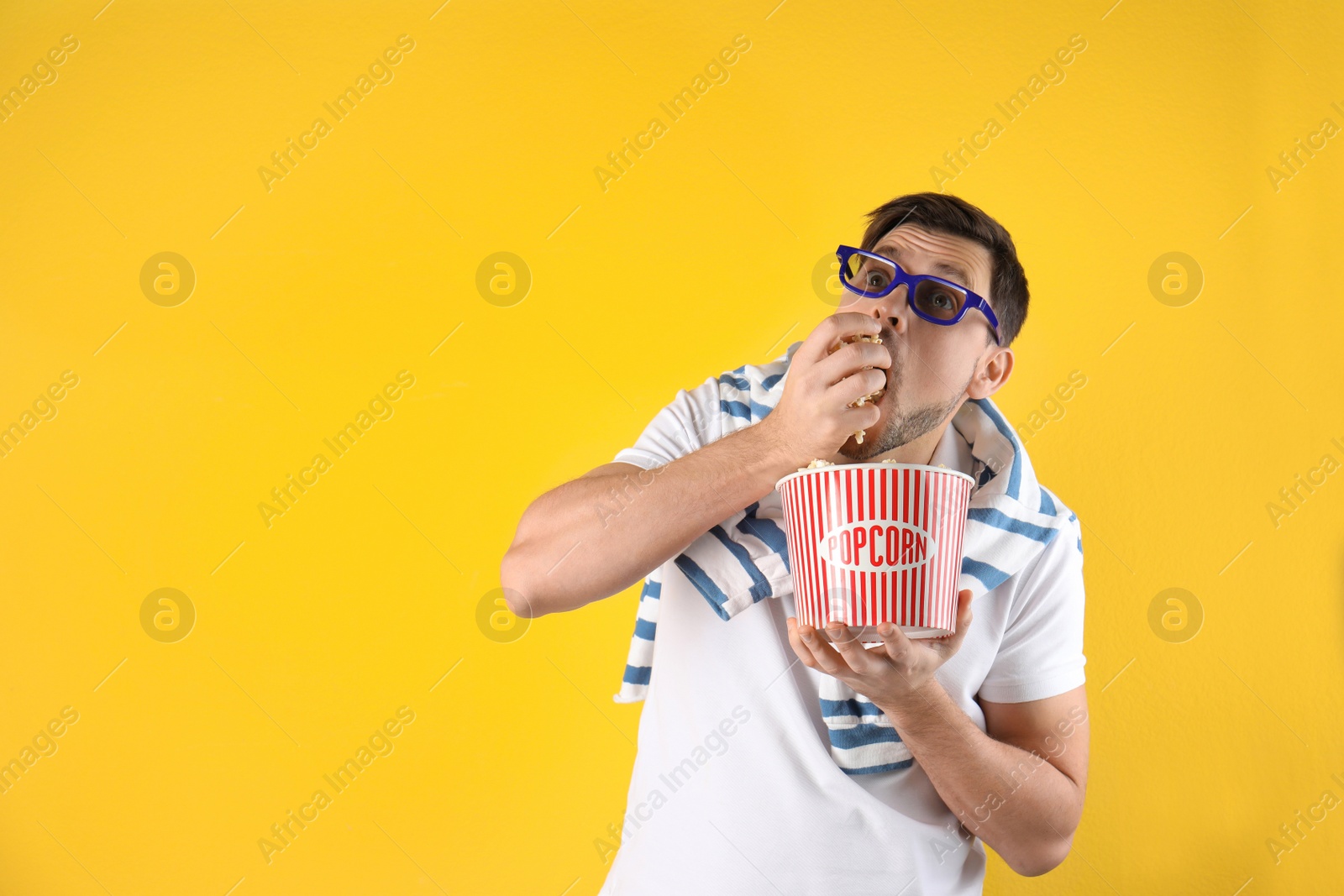 Photo of Man with 3D glasses eating tasty popcorn on color background. Space for text