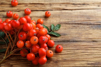 Bunch of ripe rowan berries with green leaves on wooden table, closeup. Space for text