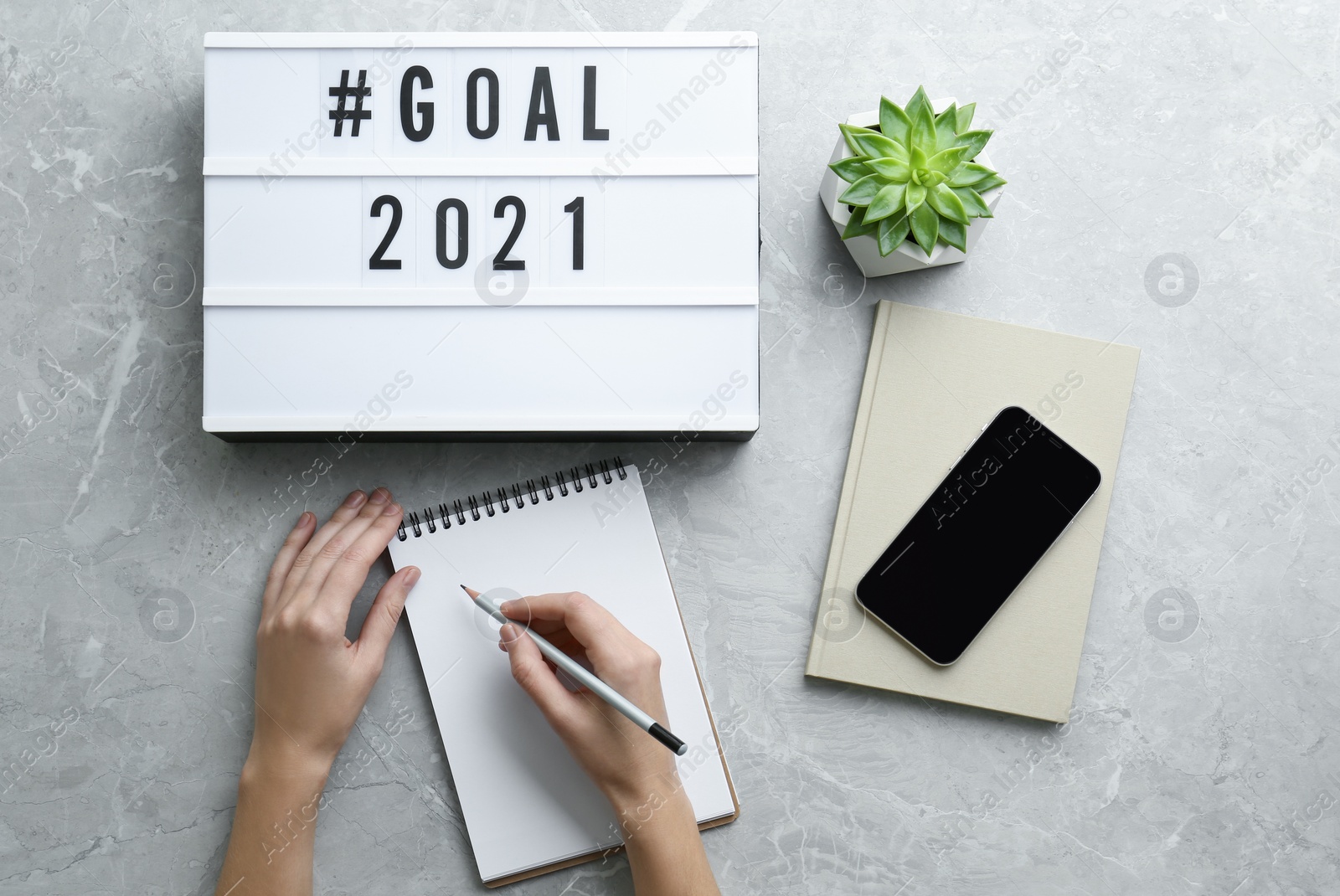 Photo of Woman writing in notebook at grey table, top view. New year targets