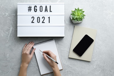 Photo of Woman writing in notebook at grey table, top view. New year targets