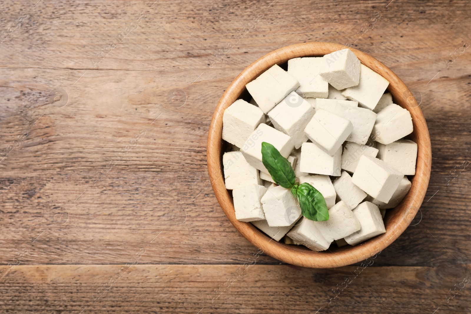 Photo of Delicious tofu with basil on wooden table, top view. Space for text