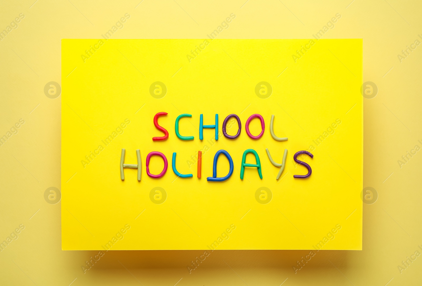 Photo of Phrase School Holidays made of modeling clay on yellow background, top view