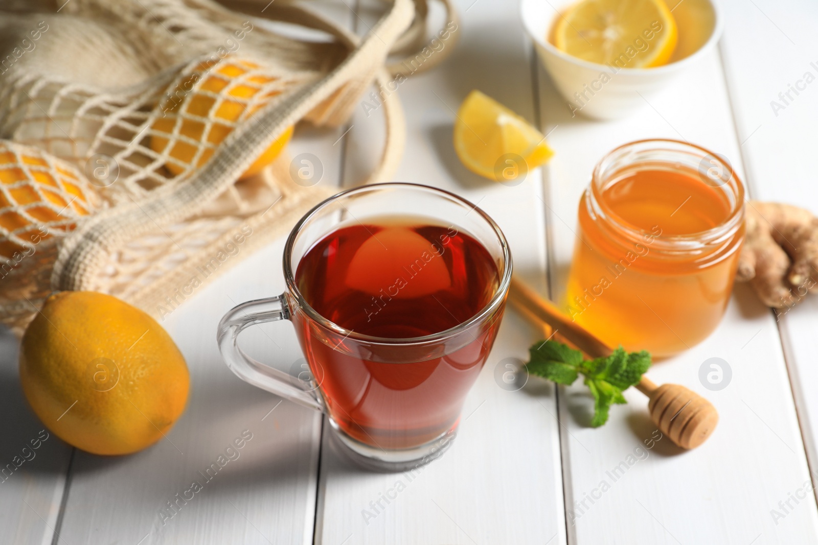 Photo of Cup of delicious ginger tea and ingredients on white wooden table