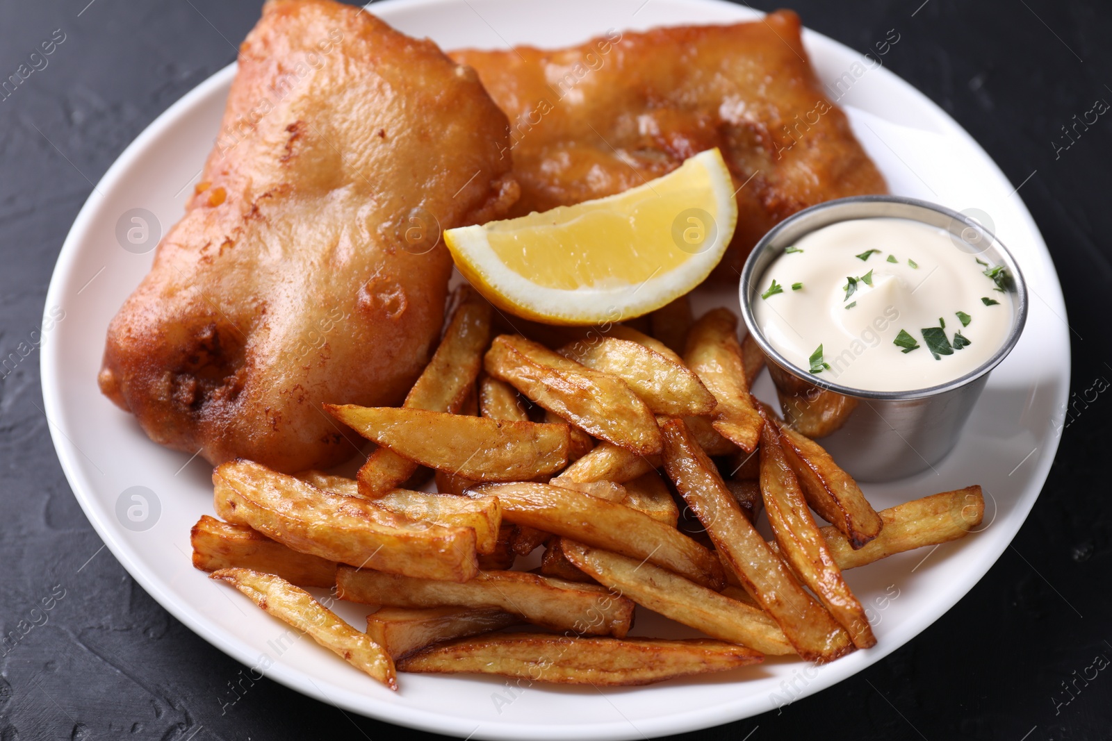 Photo of Tasty fish, chips, lemon and sauce on black table, closeup