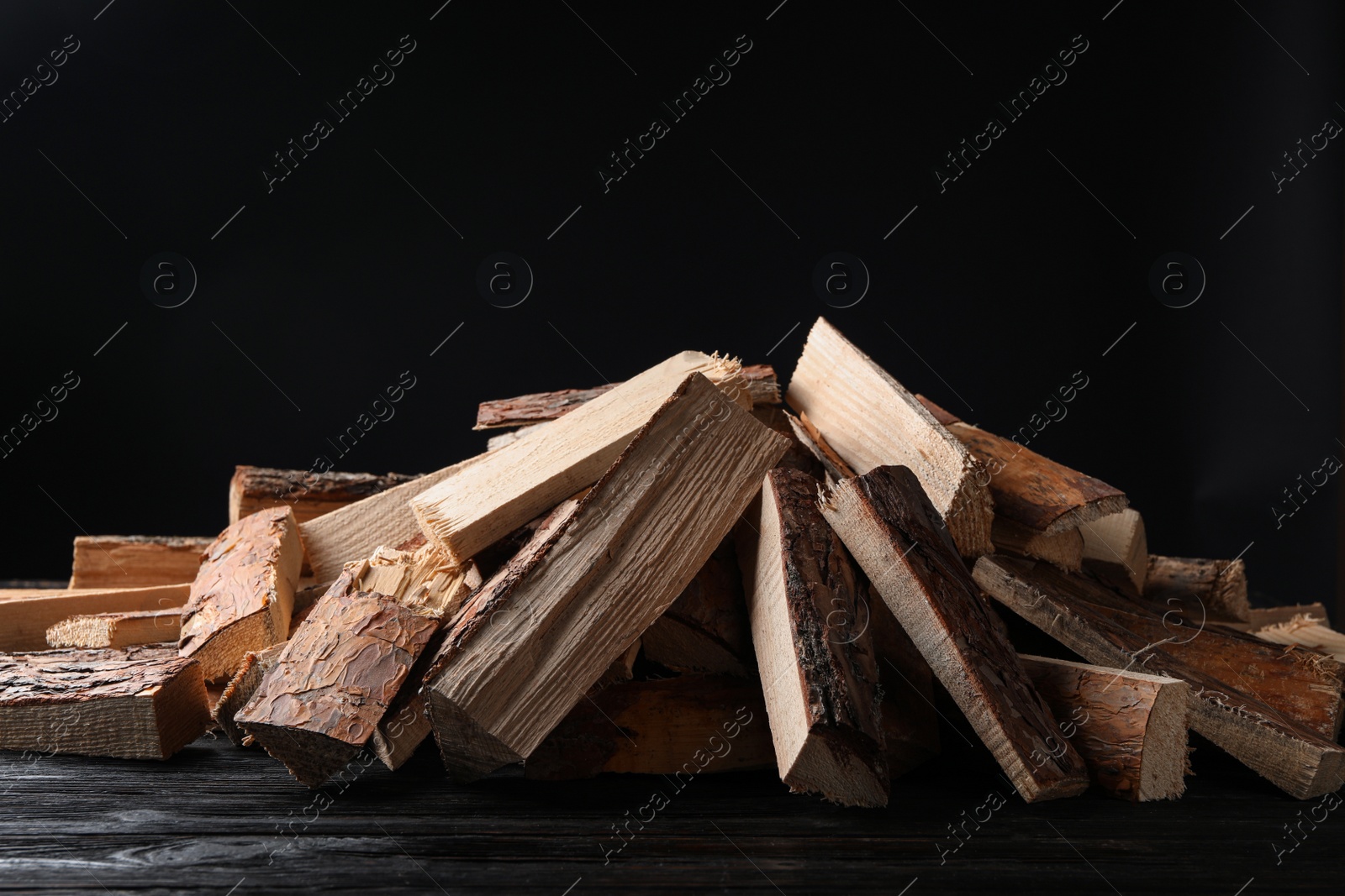 Photo of Cut firewood on table against black background