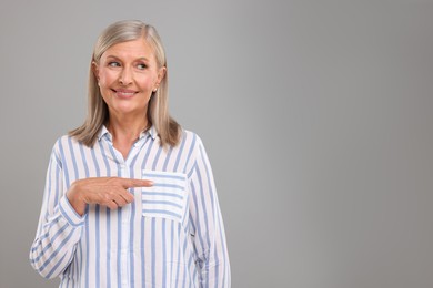 Photo of Portrait of beautiful middle aged woman pointing at something on light grey background, space for text