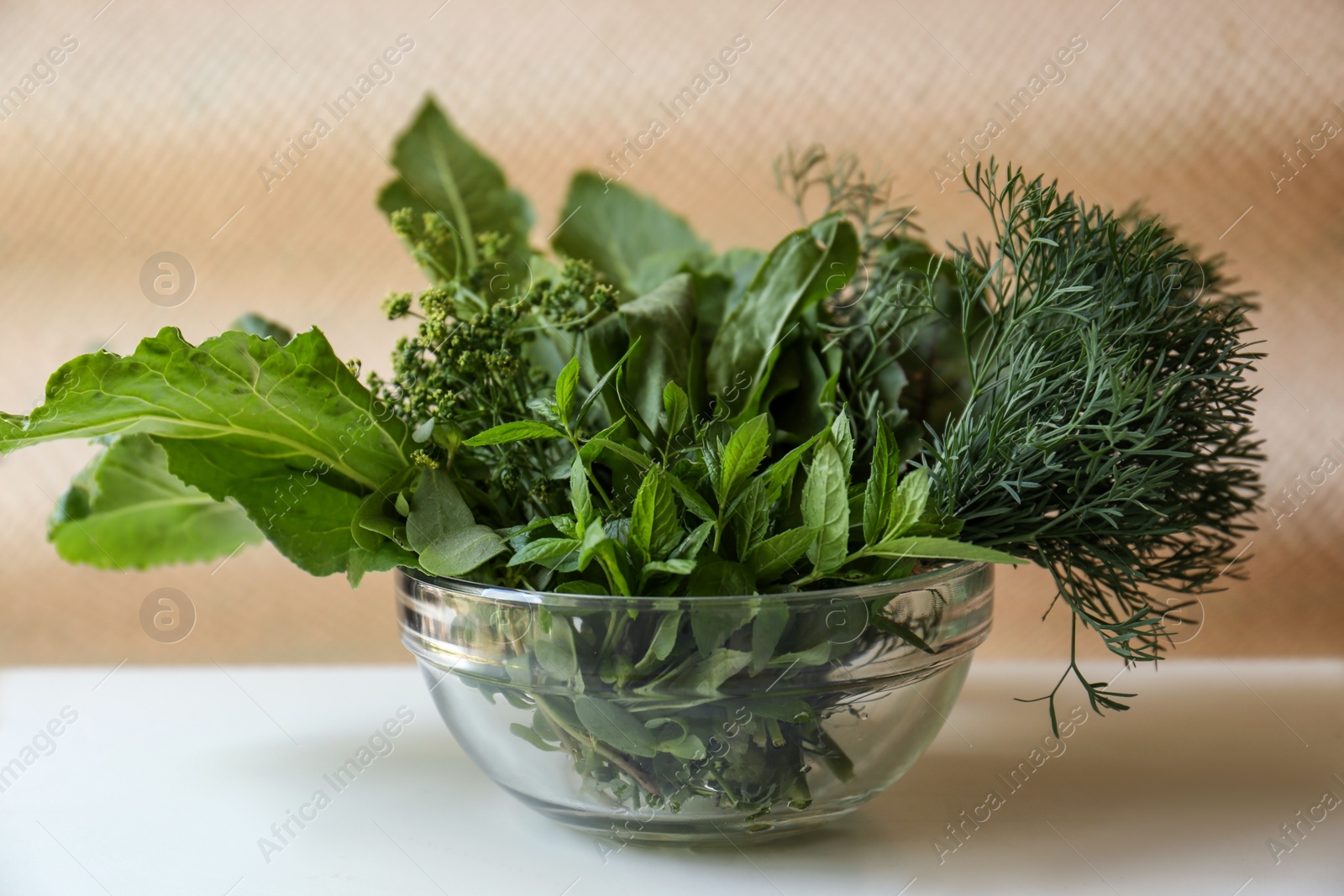 Photo of Different herbs in bowl on white wooden table