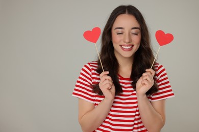 Beautiful young woman with paper hearts on grey background, space for text