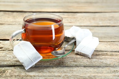 Photo of Aromatic tea in glass cup, spoon and teabags on wooden table