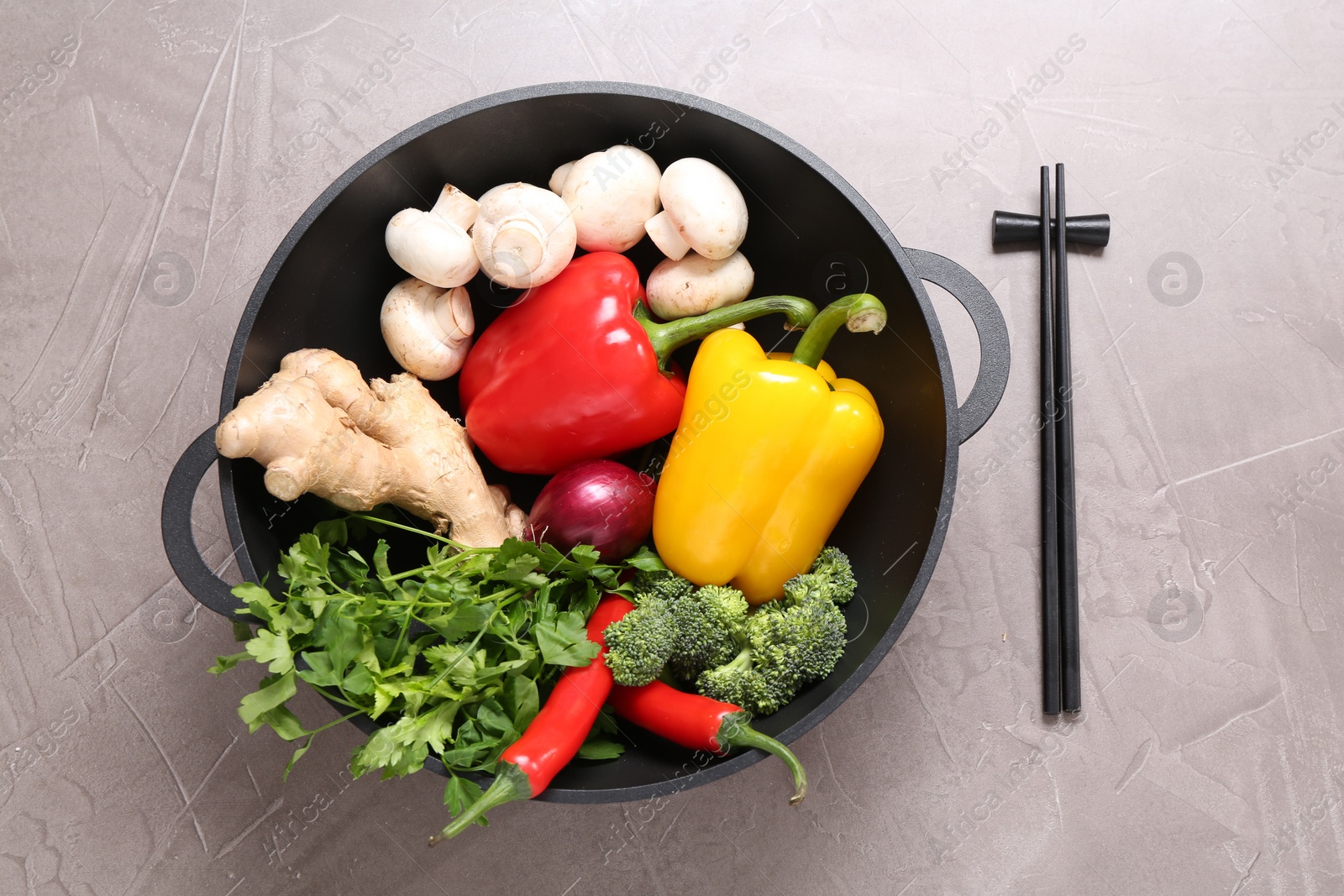 Photo of Wok, chopsticks and different products on grey textured table, flat lay