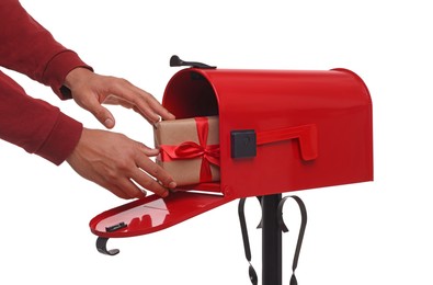 Man putting Christmas gift into mailbox on white background, closeup. Sending present by mail