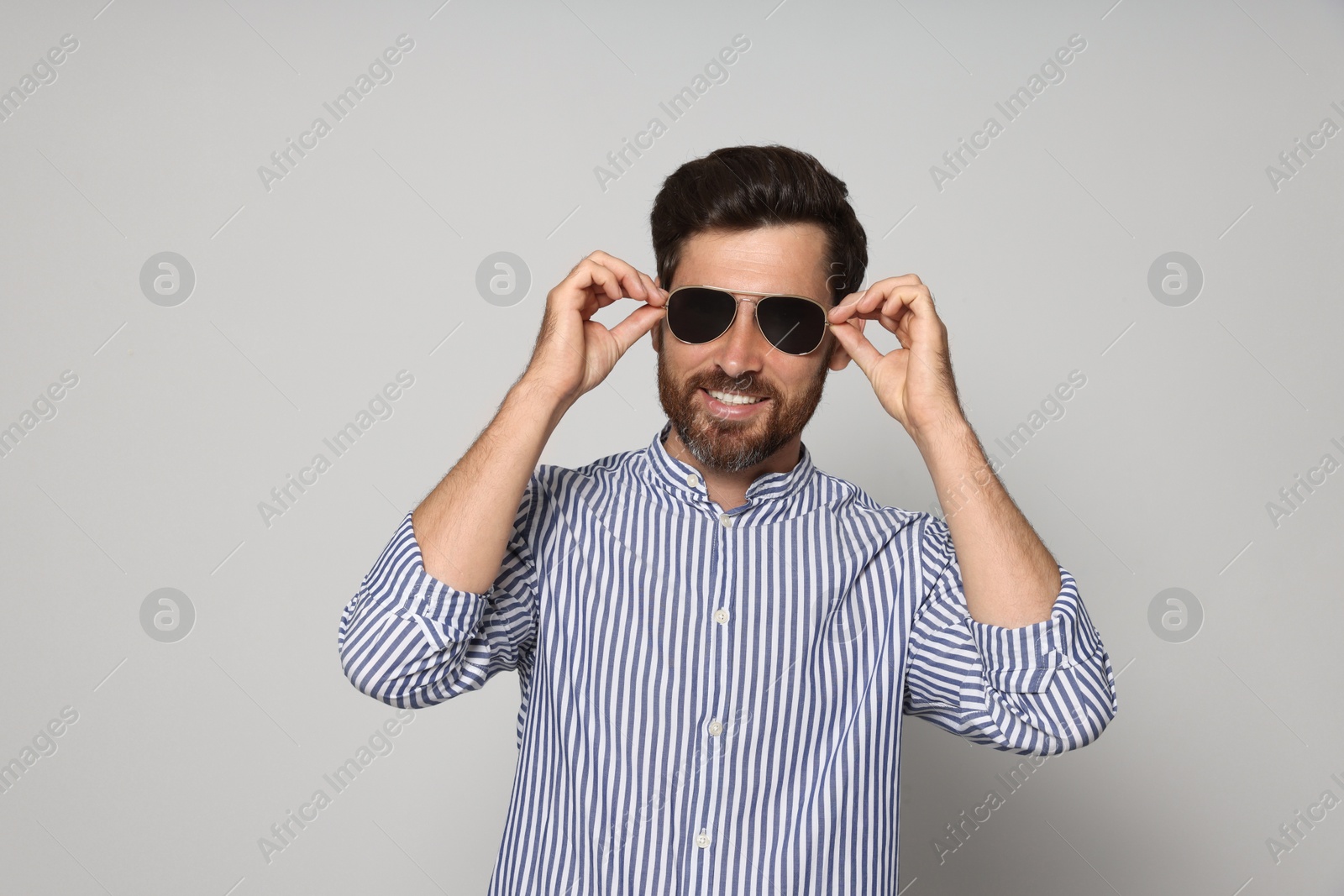 Photo of Portrait of smiling bearded man with sunglasses on grey background