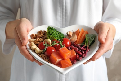 Photo of Doctor holding plate with products for heart-healthy diet, closeup