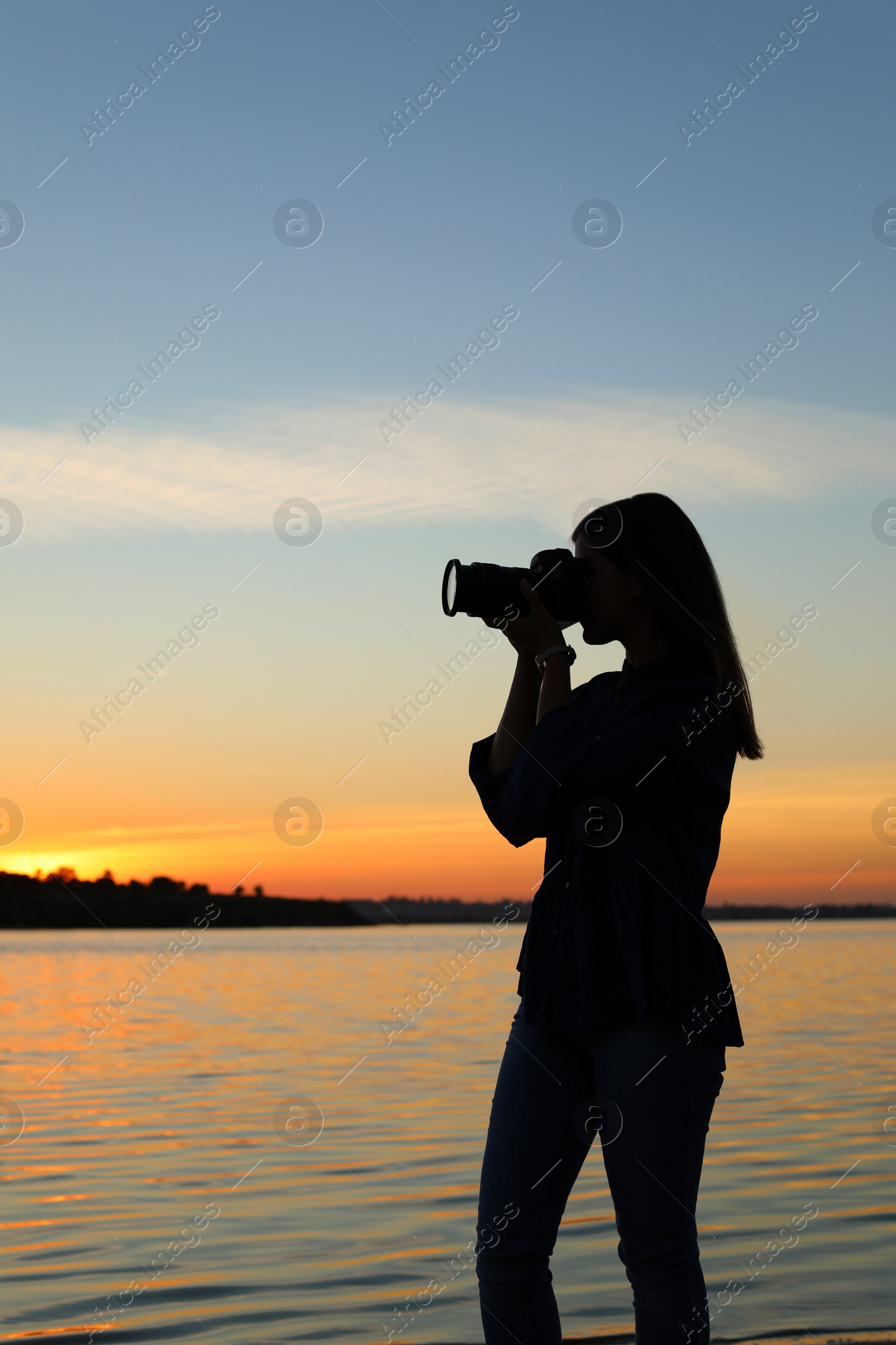 Photo of Young female photographer taking photo of riverside sunset with professional camera outdoors