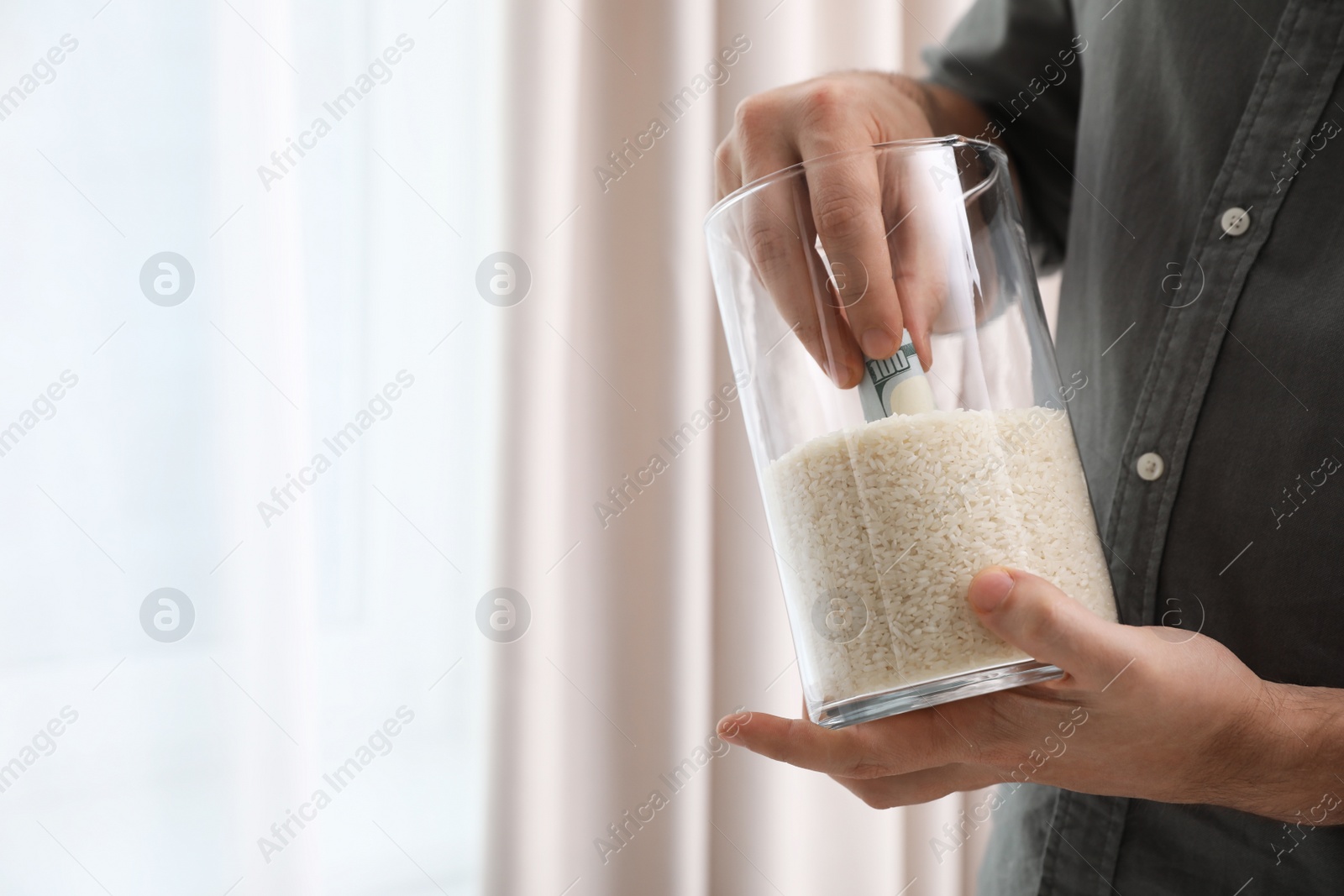 Photo of Man hiding money in jar of rice indoors, closeup with space for text. Financial savings