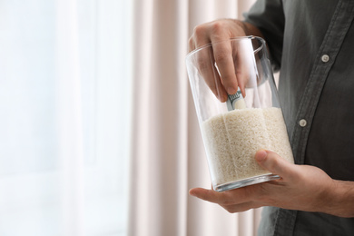 Man hiding money in jar of rice indoors, closeup with space for text. Financial savings