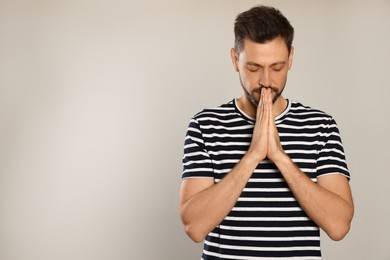 Man with clasped hands praying on light grey background. Space for text