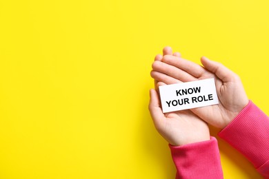 Photo of Woman holding card with phrase Know Your Role on yellow background, top view
