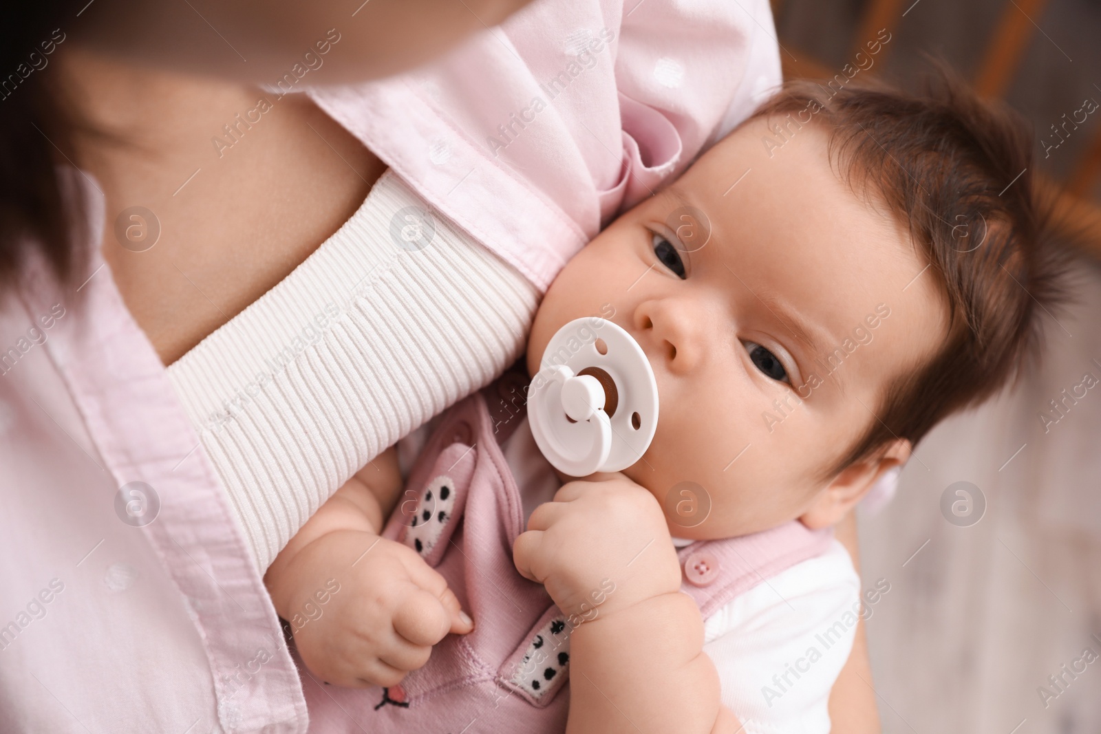Photo of Mother holding her cute little baby with pacifier on blurred background, closeup