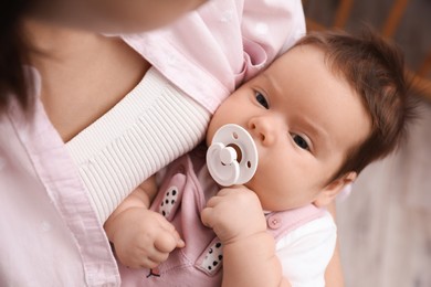 Mother holding her cute little baby with pacifier on blurred background, closeup