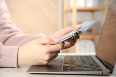 Photo of Online payment. Woman using credit card and smartphone near laptop at light grey table indoors, closeup