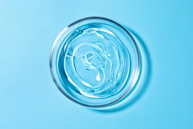 Photo of Petri dish with liquid on light blue background, top view