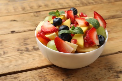 Photo of Tasty fruit salad in bowl on wooden table, closeup