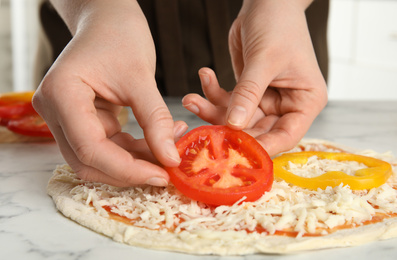 Photo of Woman adding tomato to pizza white marble table, closeup