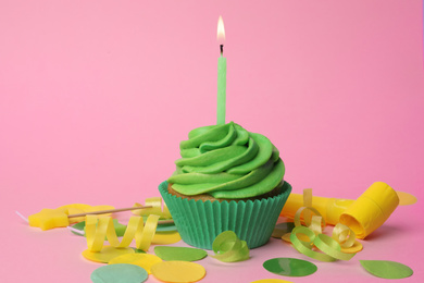 Delicious birthday cupcake with green cream and burning candle on pink background