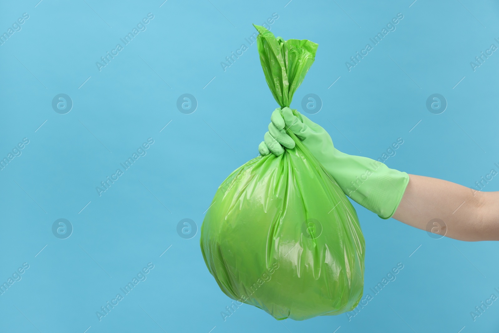 Photo of Woman holding plastic bag full of garbage on light blue background, closeup. Space for text