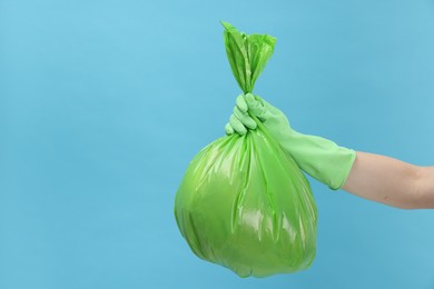 Photo of Woman holding plastic bag full of garbage on light blue background, closeup. Space for text