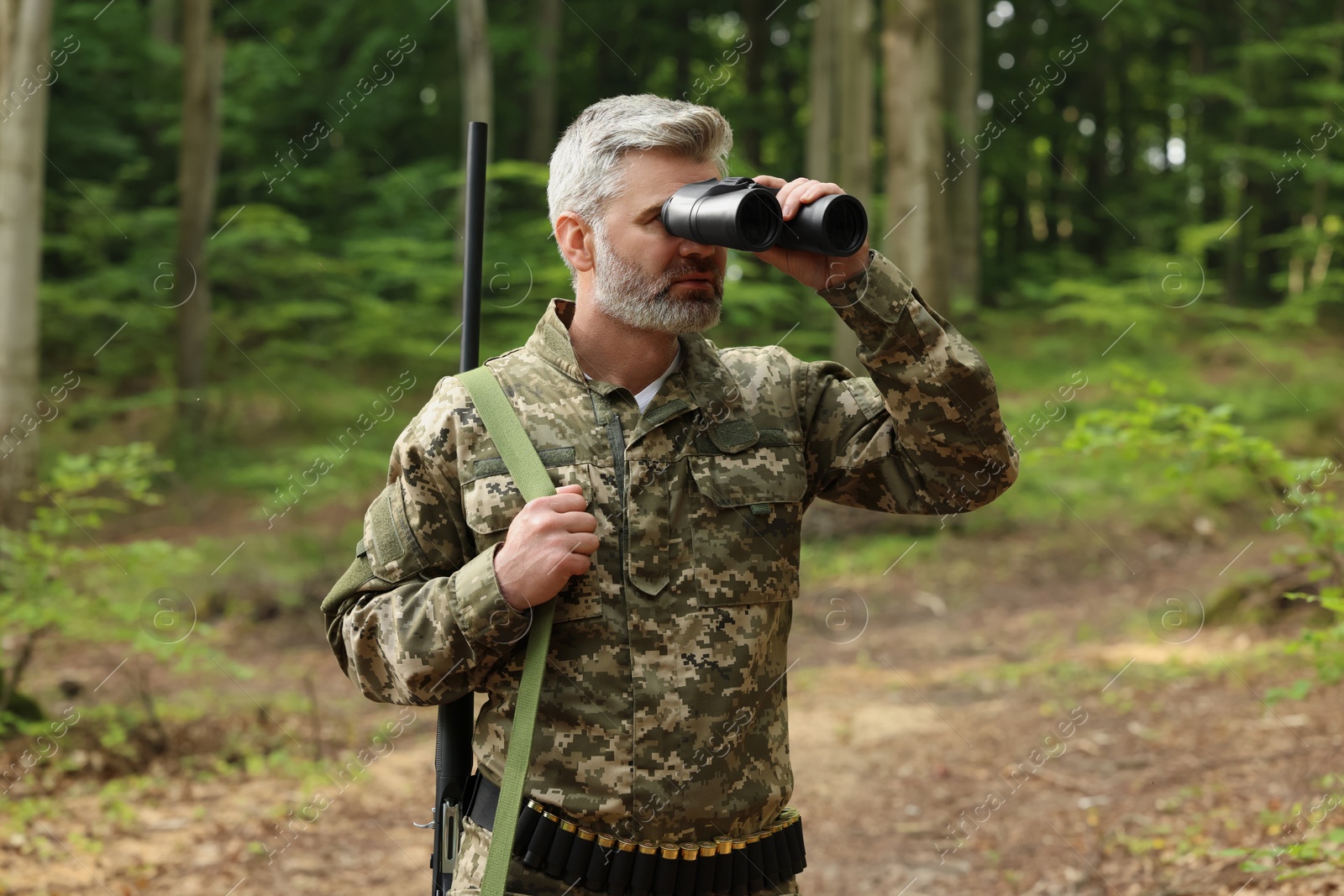 Photo of Man with hunting rifle looking through binoculars in forest