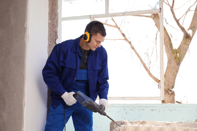 Worker using rotary drill hammer for window installation indoors