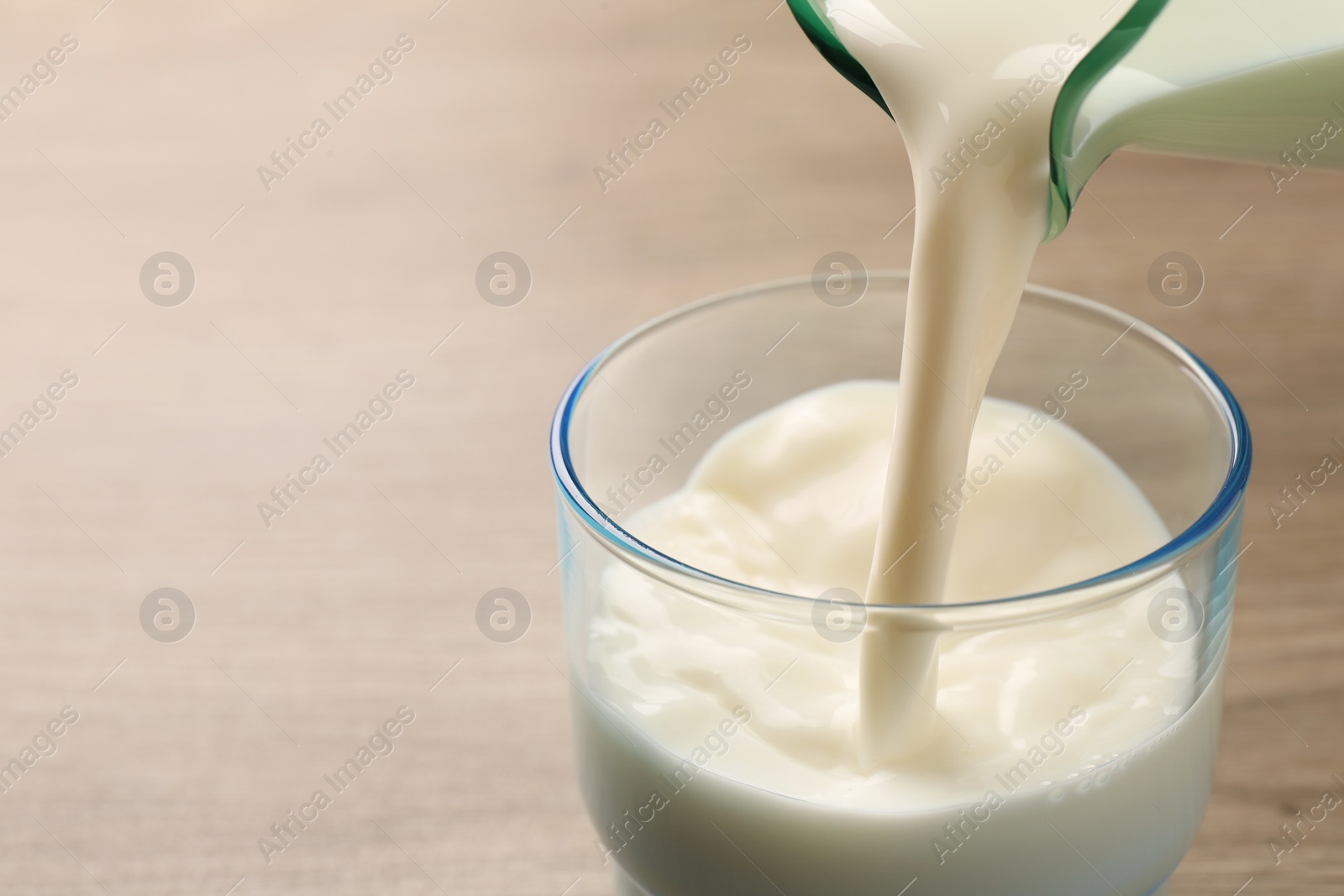 Photo of Pouring tasty milk into glass on wooden table, closeup. Space for text