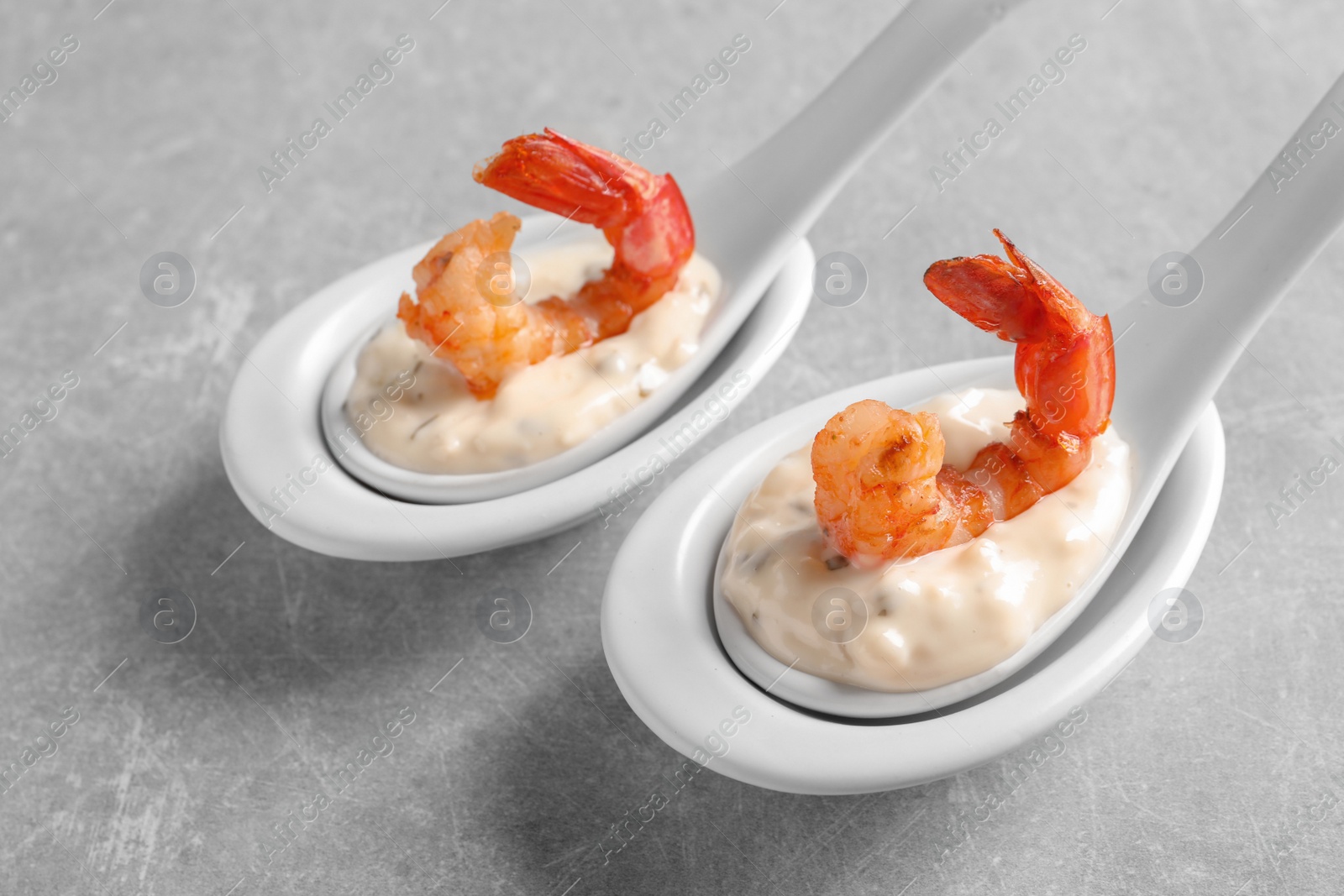 Photo of Delicious snacks with shrimp in spoons on grey background