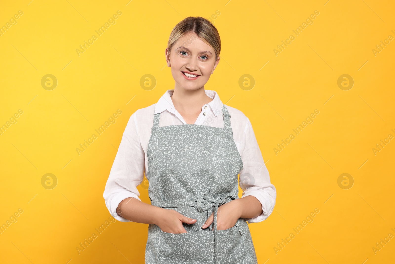 Photo of Beautiful young woman in clean apron with pattern on orange background