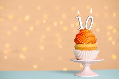 Photo of Birthday cupcake with number ten candle on stand against festive lights, space for text