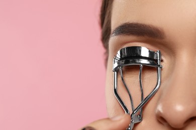 Woman using eyelash curler on pink background, closeup. Space for text